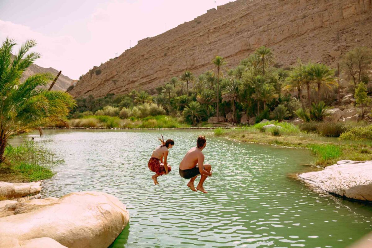 People jumping into the water of an oasis.