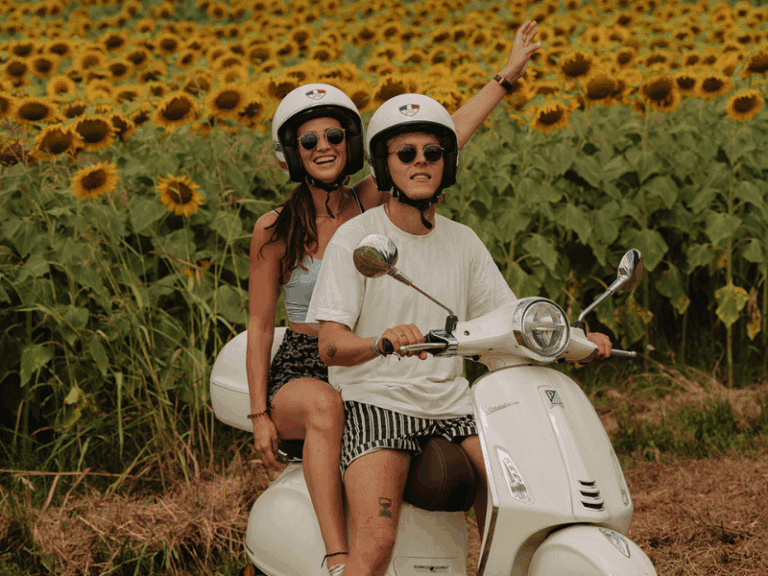 Couple sur une Vespa primavera blanche avec des tournesols en arrière-plan.