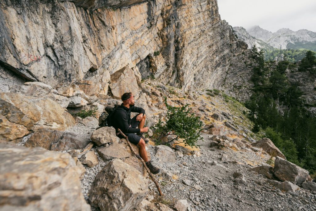 Randonneur die een pauze neemt om van het uitzicht te genieten tijdens een wandeling in de Balkan in Albanië richting Theth.