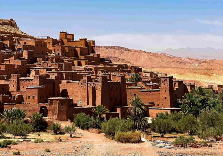View of Ait Ben Haddou in Morocco, with its famous earthen kasbahs and palm trees in the foreground.